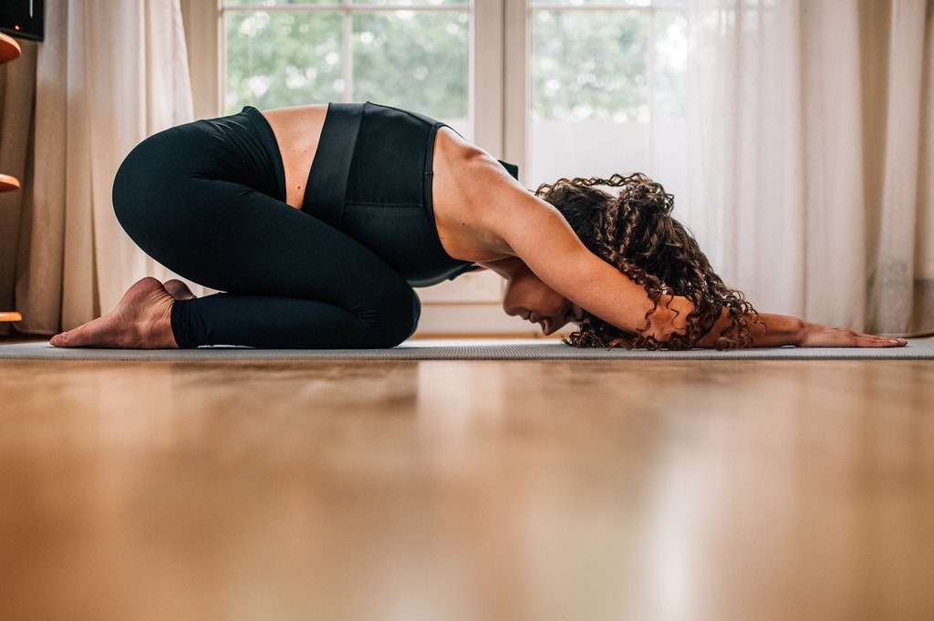 A woman stretching on a yoga mat beside a sunlit window